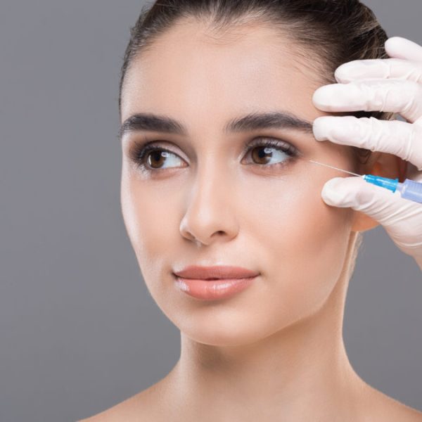 Women face care. Portrait of attractive young woman making cosmetic injections on grey background, closeup, empty space